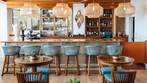 A bar area with wooden bar stools, round tables, and hanging wicker chandeliers. - Kaimana Beach Hotel (Honolulu)