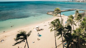 A beach with clear turquoise water, palm trees, and a lifeguard tower. - Kaimana Beach Hotel (Honolulu)