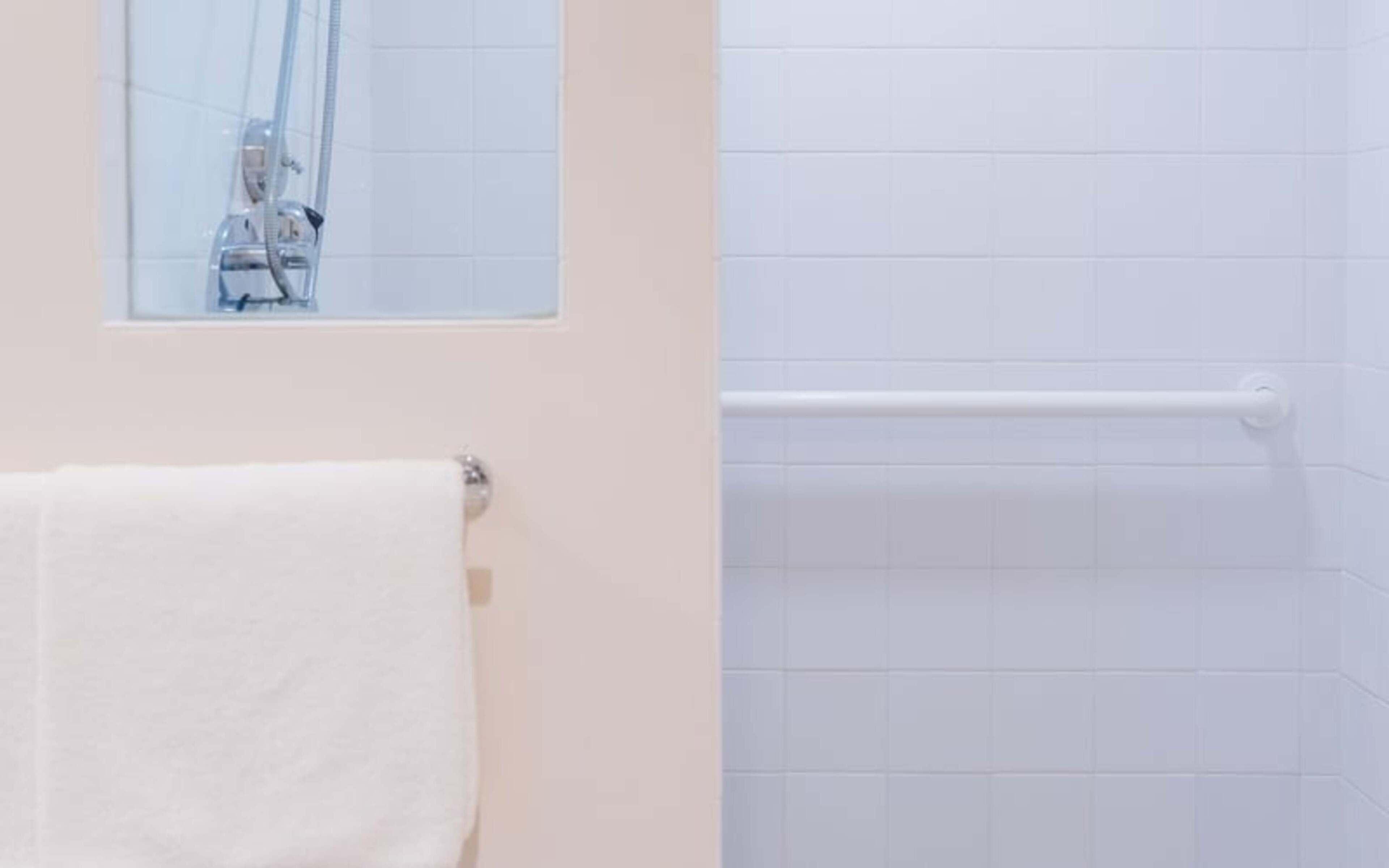 Un baño con una toalla blanca en un perchero, una ducha con puerta de cristal y una pared de azulejos blancos.