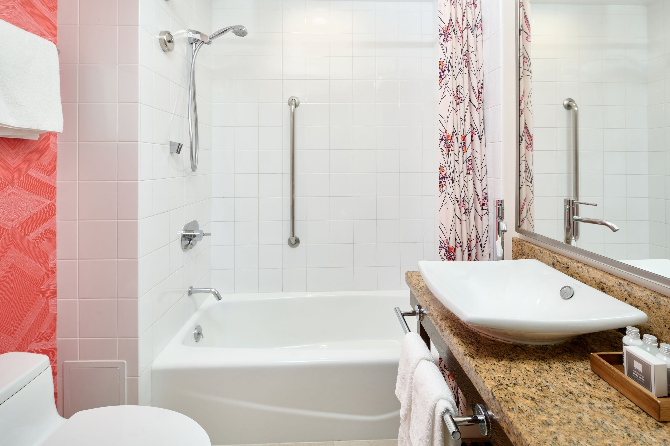 A modern bathroom with a white bathtub, a sink with a granite countertop, and a shower with a handrail.