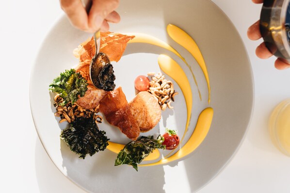 A plate of food with various items including greens, nuts, and a piece of meat, arranged on a white plate with yellow accents. - Kaimana Beach Hotel (Honolulu)