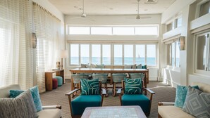 A spacious living room with a large window overlooking the sea, furnished with teal and beige sofas, a wooden coffee table, and a dining area with wooden chairs and a table. - Kaimana Beach Hotel (Honolulu)