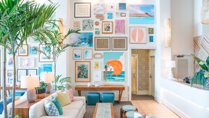 A spacious living room with a sofa, coffee table, and chairs, decorated with framed artwork and plants. - Kaimana Beach Hotel (Honolulu)
