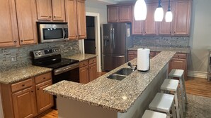 Una cocina moderna con encimeras de granito, electrodomésticos de acero inoxidable, armarios de madera y una isla integrada con taburetes de bar.