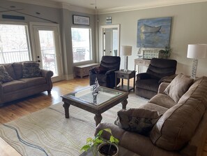 A living room with a beige sofa, a glass coffee table, and a potted plant. There is a painting on the wall and a sign that reads "The Snug Family Lake Condo." - Spacious Condo at Lake Martin, AL (Dadeville)