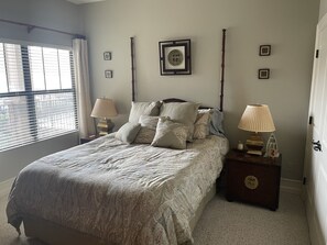 A bedroom with a bed, two bedside tables with lamps, a framed picture on the wall, and a window with blinds.