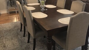 Un comedor con mesa de madera oscura, sillas color beige y una lámpara colgante moderna.