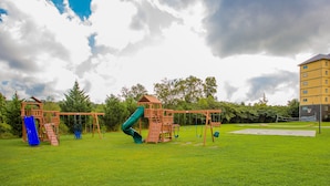 A playground with a slide and swings, surrounded by grass and trees, with a building in the background. - Location, location, location! 2br/2bath condo in the heart of Pigeon Forge (Pigeon Forge)
