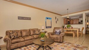A living room with a brown leather sofa, a round coffee table, and a patterned rug. There is a dining area with a wooden table and chairs in the background. - Location, location, location! 2br/2bath condo in the heart of Pigeon Forge (Pigeon Forge)