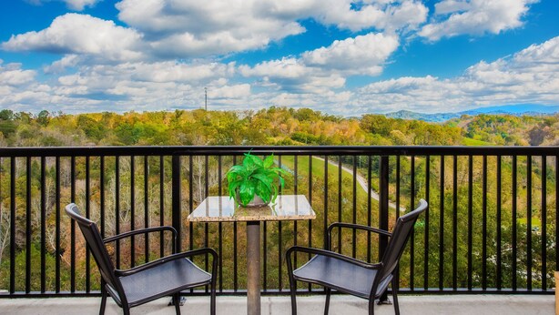 A balcony with two chairs and a table, a potted plant, and a scenic view of trees and hills. - Location, location, location! 2br/2bath condo in the heart of Pigeon Forge (Pigeon Forge)