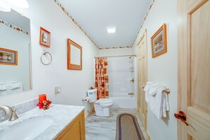 A bathroom with a white sink, toilet, and bathtub. There are framed pictures on the walls and a towel rack with towels. - Gorgeous Lakefront Home with a Fire Pit, Two Living Areas, and a Sunroom (Chestertown)