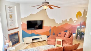 Ett vardagsrum med en öppen spis, en tv, en soffa och en takfläkt.