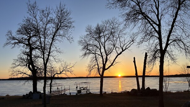 A lakeside view with a wooden deck, bare trees, and a sunset over the water. - Enjoy Lake Life, A Great Minnesota Getaway! (Henning)