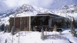 Ein modernes Gebäude mit Glasfassade, umgeben von schneebedeckten Bergen und vereinzelten Bäumen.
