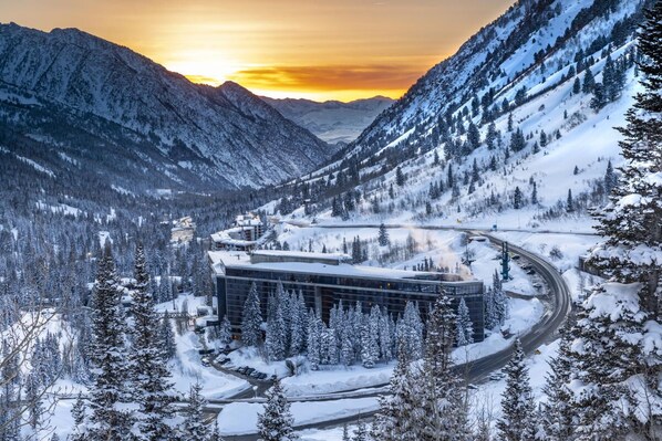 A modern building with a curved driveway, surrounded by snow-covered mountains and trees.