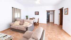 A living room with a sofa, a dining table, and a ceiling fan. - Chalet rustic Roche with pool (CONIL DE LA FRONTERA)