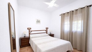 A bedroom with a bed, nightstands, a mirror, a ceiling fan, a window with curtains, and a wall-mounted bicycle artwork. - Chalet rustic Roche with pool (CONIL DE LA FRONTERA)