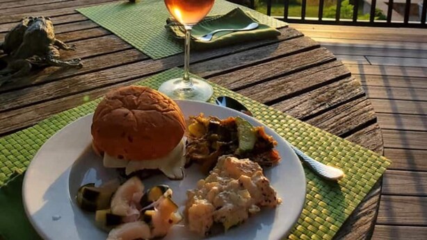 Eine Holzterrasse mit Tisch, der für eine Mahlzeit gedeckt ist, einem Weinglas und einem malerischen Sonnenuntergang.
