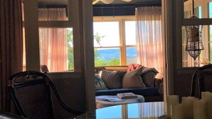 Ein gemütliches Zimmer mit Meerblick, einem Deckenventilator, einer Couch mit Kissen und einem Tisch mit Kerzen.