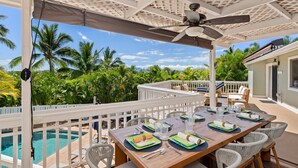 An outdoor dining area with a pool, white railings, and a ceiling fan.