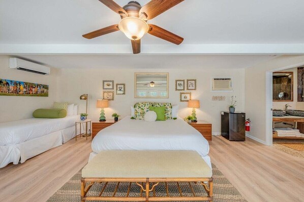 A bedroom with a large bed, a smaller bed, a ceiling fan, and a nightstand with a lamp.