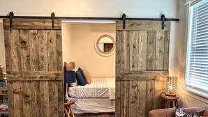 Ein Schlafzimmer mit einem Bett, einem runden Spiegel, einer Schiebetür im Scheunenstil, einem kleinen Holzschemel und einer Lampe.