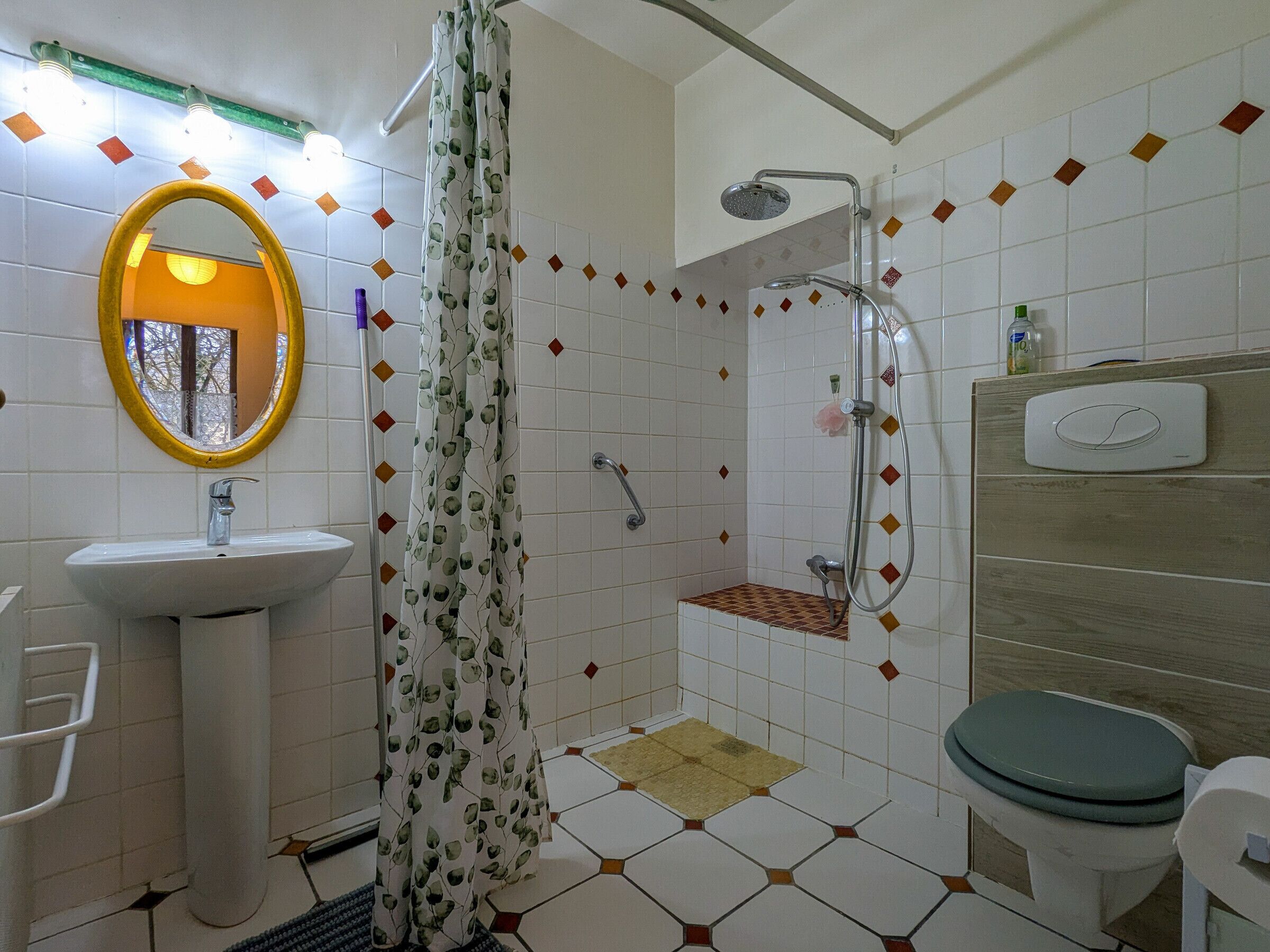 Un baño con ducha, lavamanos, inodoro y un espejo con marco amarillo.