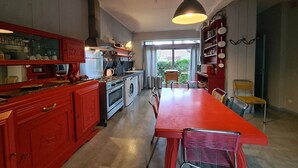 Een moderne keuken met rode kastjes, roestvrijstalen apparatuur en een grote eettafel.