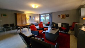 Een moderne woonkamer met een eettafel, rode en zwarte stoelen, een rood tapijt en uitzicht door grote ramen.