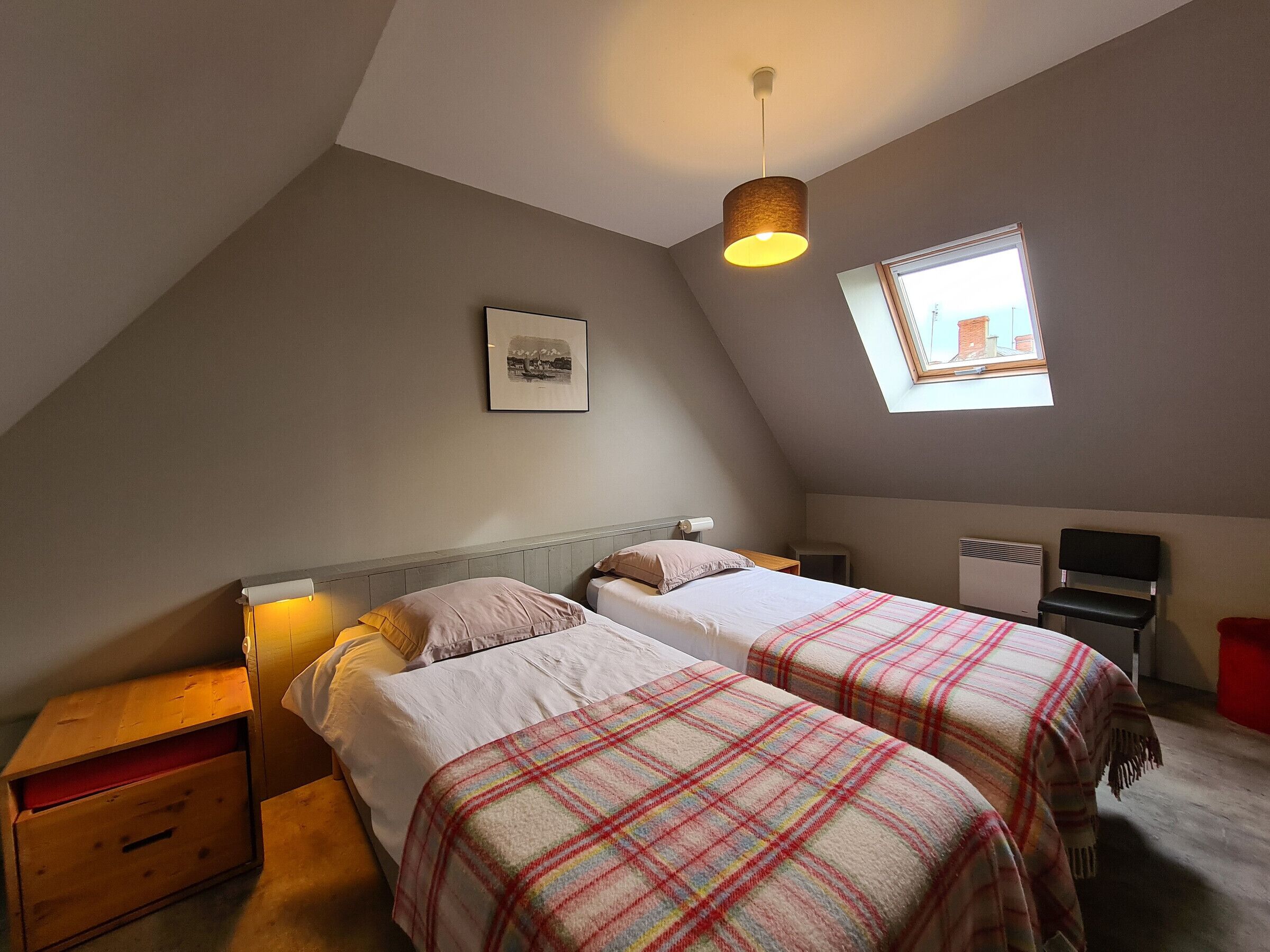Una camera da letto mansardata accogliente con due letti, un velux, un quadro incorniciato e un piccolo termosifone.