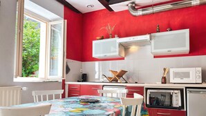 Une cuisine aux murs rouges, aux armoires blanches et à la table recouverte d’une nappe à motifs floraux.