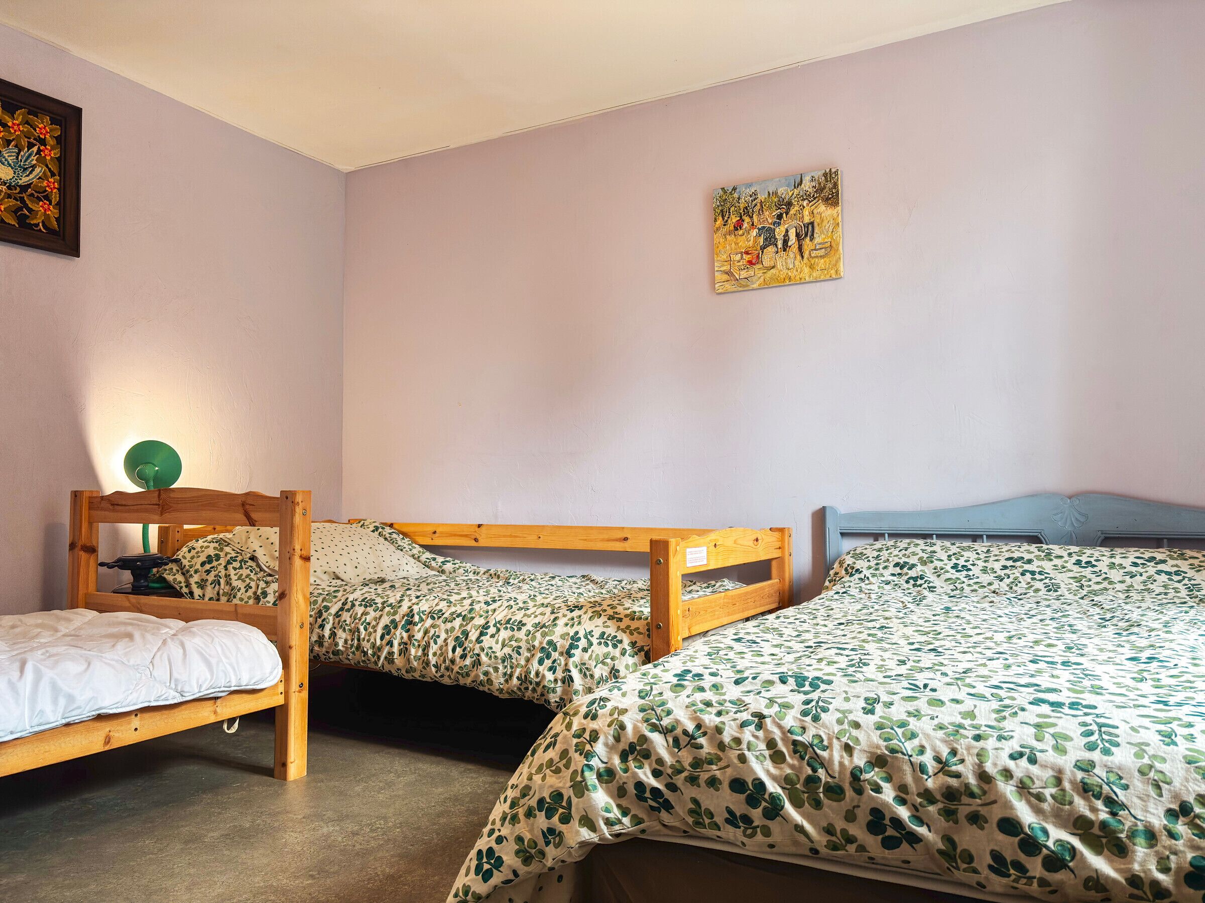 A bedroom with two wooden beds, a green lamp, and a painting on the wall.