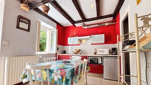 Une cuisine aux murs rouges, aux armoires blanches et dotée d’un coin repas avec une table recouverte d’une nappe à motifs floraux.