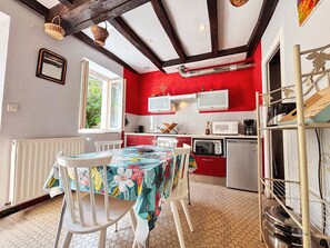 A kitchen with red walls, white cabinets, and a dining area with a table covered in a floral tablecloth. - Charming Cottage in Berry: Fireplace, Near Golf & Spa, Sleeps 6, Parking Included (Briantes)