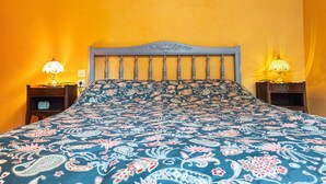 Un lit recouvert d’une couvre-lit à motifs floraux, deux lampes de chevet et un tableau accroché au mur.