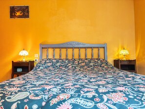 A bed with a floral-patterned bedspread, two bedside lamps, and a wall-mounted picture. - Charming Cottage in Berry: Fireplace, Near Golf & Spa, Sleeps 6, Parking Included (Briantes)