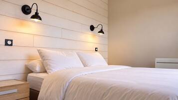 Un dormitorio con cabecera de madera, dos lámparas de noche, una cama con ropa de cama blanca y una mesita de noche con cajones.