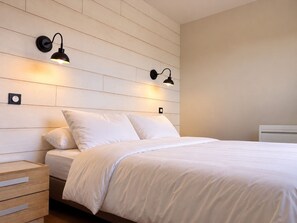 Une chambre à coucher avec une tête de lit en bois, deux lampes de chevet, un lit avec une literie blanche et une table de chevet avec des tiroirs.