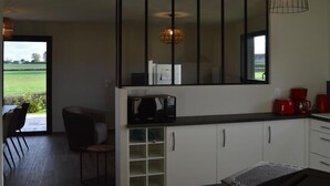 Een moderne keuken met witte kasten, een zwart aanrecht en een grote spiegel boven de gootsteen. Door een open deur is een eethoek met een tafel en stoelen te zien.