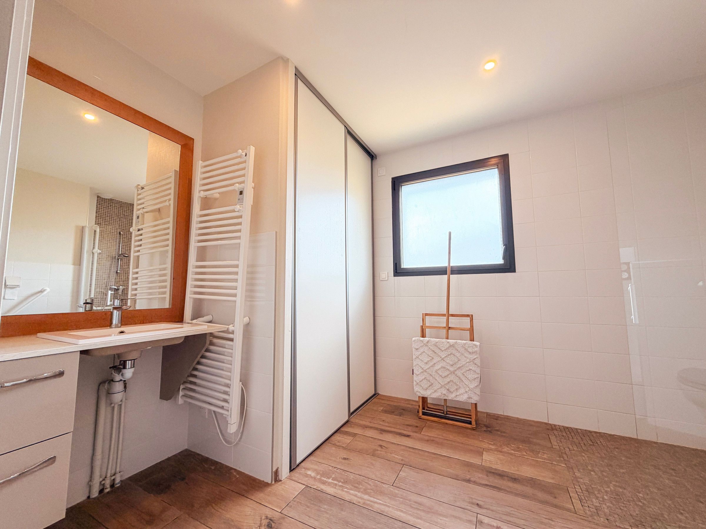 Ein modernes Badezimmer mit Duschkabine, Spiegel, Handtuchhalter und Fenster.