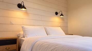 A bedroom with a wooden headboard, two bedside lamps, a wooden nightstand with drawers, and a bed with white bedding.