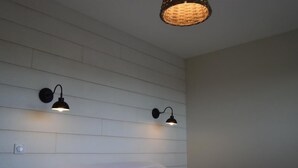 Een slaapkamer met een bed, twee wandlampen en een geweven plafondlamp.