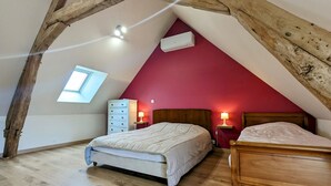 A bedroom with a sloped ceiling, a skylight, a red wall, two bedside tables with lamps, and two beds. - Charming Berry Home near Zoo de Beauval & Medieval Loches, Private Parking, Shared Garden (Arpheuilles)