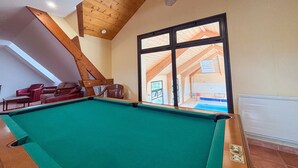 A pool table in a room with wooden beams and a large window.