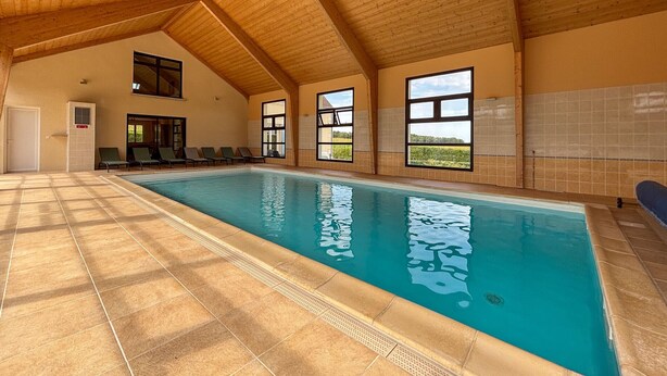 A large indoor swimming pool with tiled floors and wooden beams on the ceiling.
