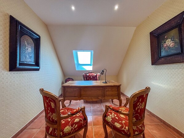 A dining area with a wooden table and two chairs, a small window, and framed artwork on the walls.