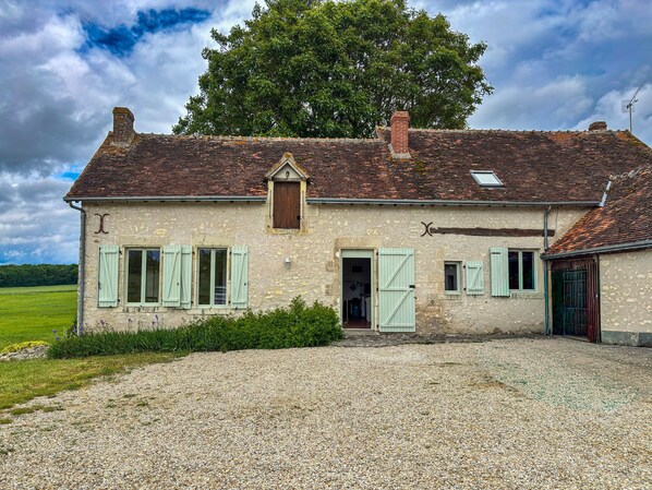 A two-story stone house with a tiled roof, a wooden door, and a gravel driveway.