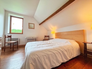 A bedroom with a bed, wooden floor, a window, a chair, a desk, and a lamp.