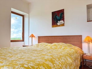 A bedroom with a bed, a window, a painting, and a lamp.