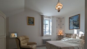 A bedroom with a large bed, a chair, a window with curtains, a wall-mounted lamp, and two framed pictures. - Charming Stone House with Terrace, Kids’ Playground, and Equestrian Space in Scenic Berry (Pérassay)